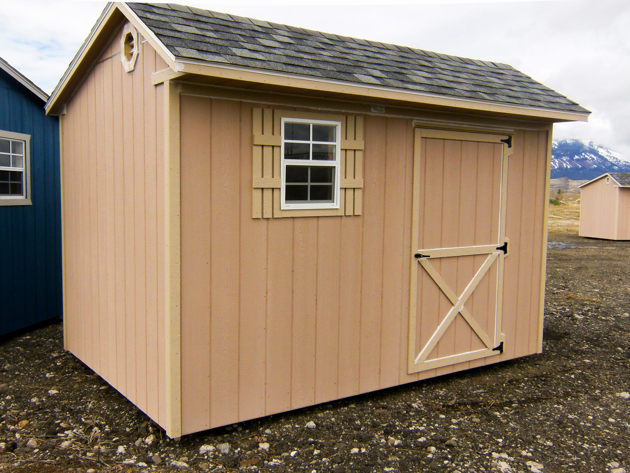 One of our peach 6x12 Quaker Sheds for sale with beige trimmed door and white-framed window with beige shutters beneath dark gray roof on lot