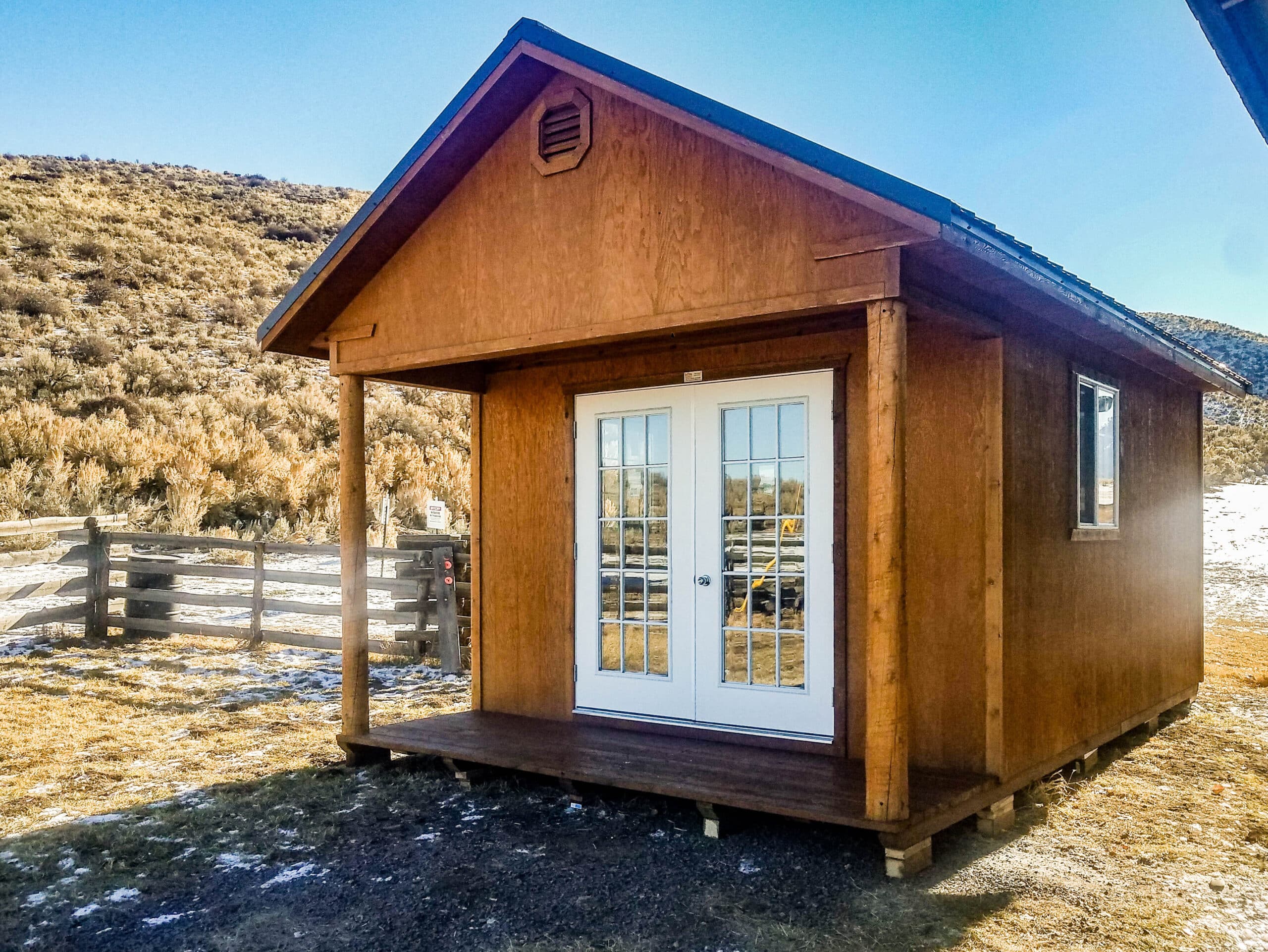 Wooden shed with a porch, double doors, and side windows - perfect for your tiny home shed ideas.